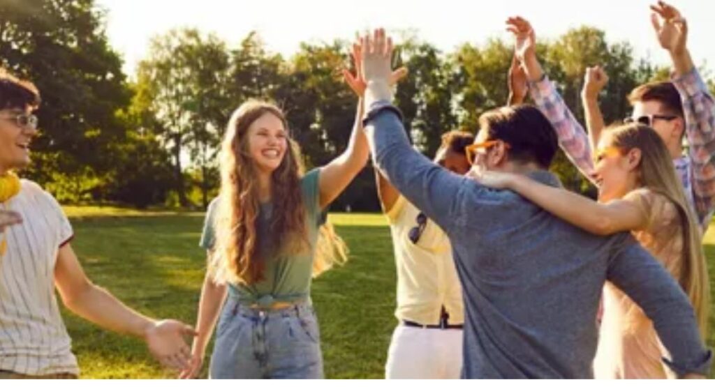 Happy friends exchanging cards and gifts outdoors in a park, celebrating friendship and sharing joyful moments.